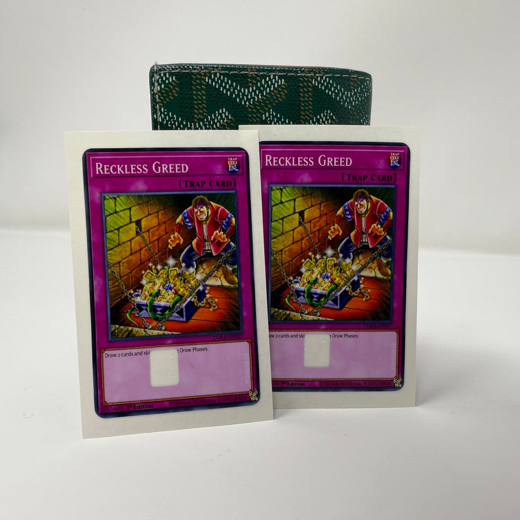 Single Reckless Greed Yu-Gi-Oh! credit card sticker displayed at angle against green patterned wallet, showcasing detailed trap card artwork with figure hunched over treasure and authentic purple card border from Kibakiba.co